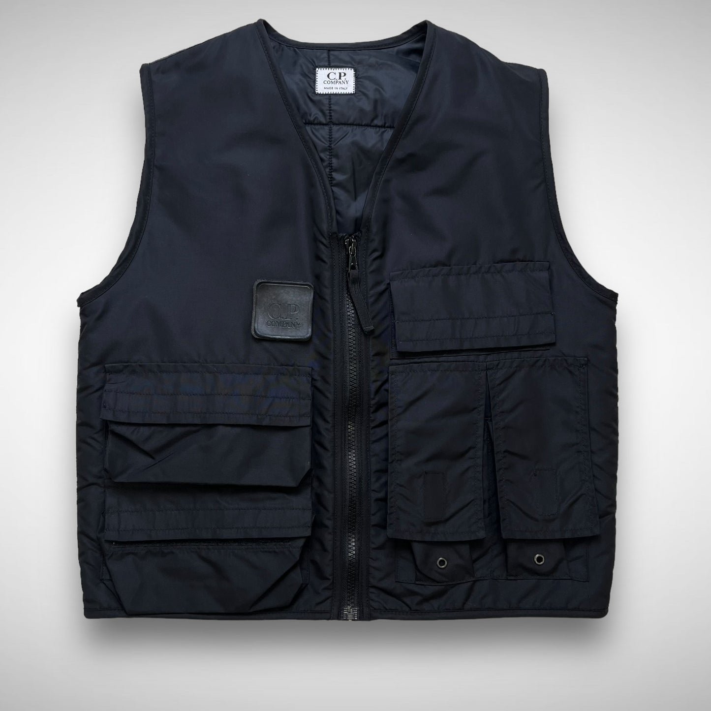 A black CP Company 'Urban Protection' Utility Vest with multiple velcro pockets and a rubber velcro patch on the front.